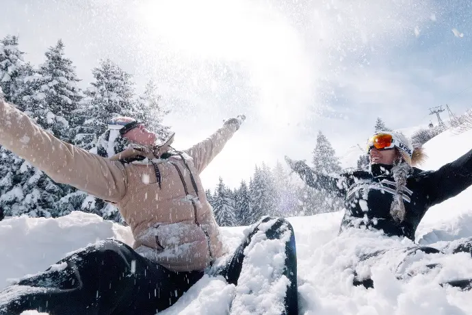 Deux personnes jouant dans la neige sous un ciel ensoleillé, illustrant comment la vidéo transmet des émotions authentiques et crée une connexion visuelle.