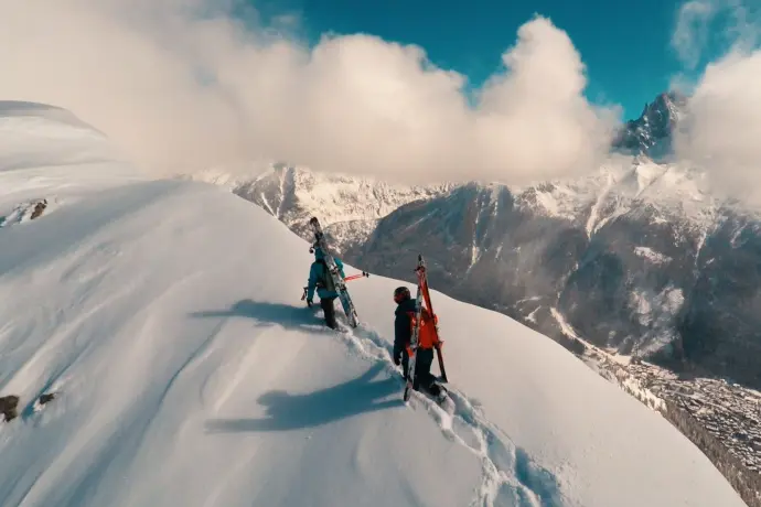 Prise de vue aérienne de deux skieurs en montagne enneigée, illustrant l'efficacité des drones pour capturer des événements sportifs avec des perspectives dynamiques.